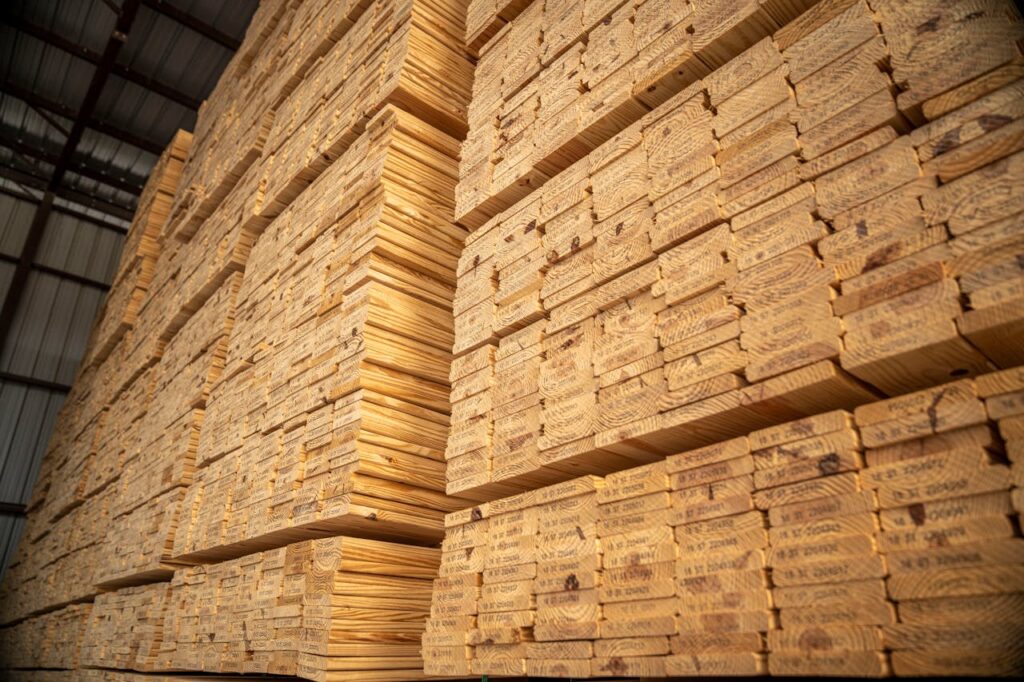 Large stacks of lumber stored in an industrial warehouse, showcasing woodworking materials.